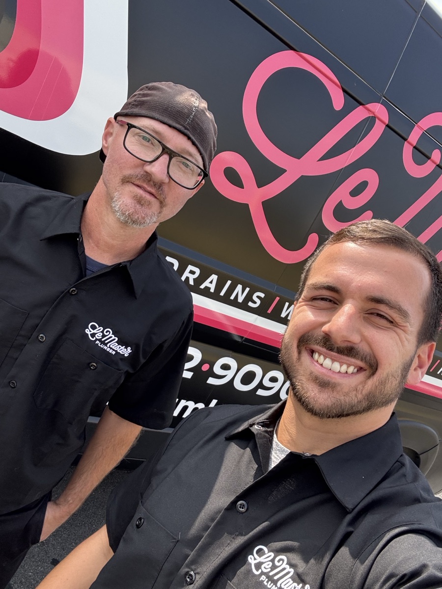 Two LeMaster Plumber technicians smiling in front of a LeMaster service van